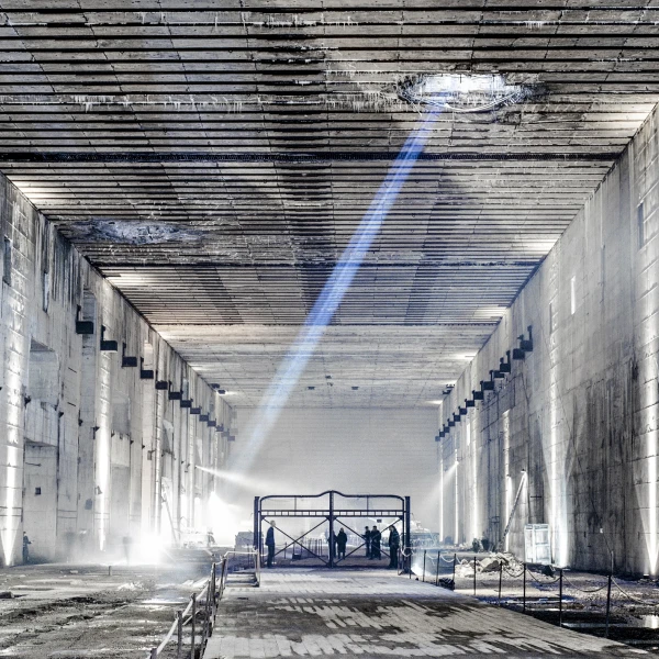 Das Foto zeigt den Ruinenteil des Bunker Valentin von innen. Im Ruinenteil stehen Menschen auf einem Gestell und ein blauer Lichtstrahl aus einem Durchschlagskrater zieht durch das Bild. Die Menschen führen die Aufführung "Die letzten Tage der Menschheit" (2001) auf  