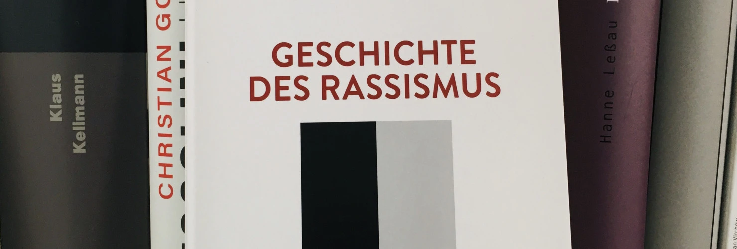 Ein Bild des Buches "Geschichte des Rassismus" von Christian Geulen mit einem Hintergrund aus Büchern.   