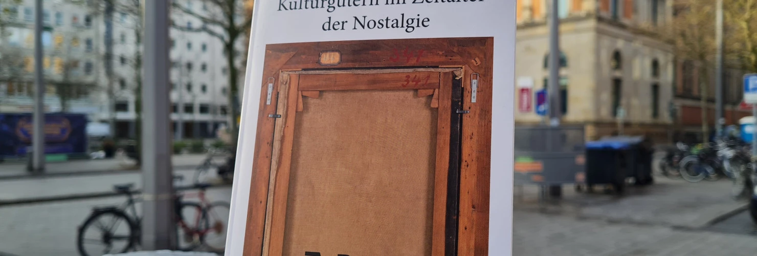 Ein BIld des Buches: " Was soll zurück? Die Restitution von Kulturgütern im Zeitalter der Nostalgie" von Sophie Schönberger mit dem Hintergrund einer städtischen Straße.  