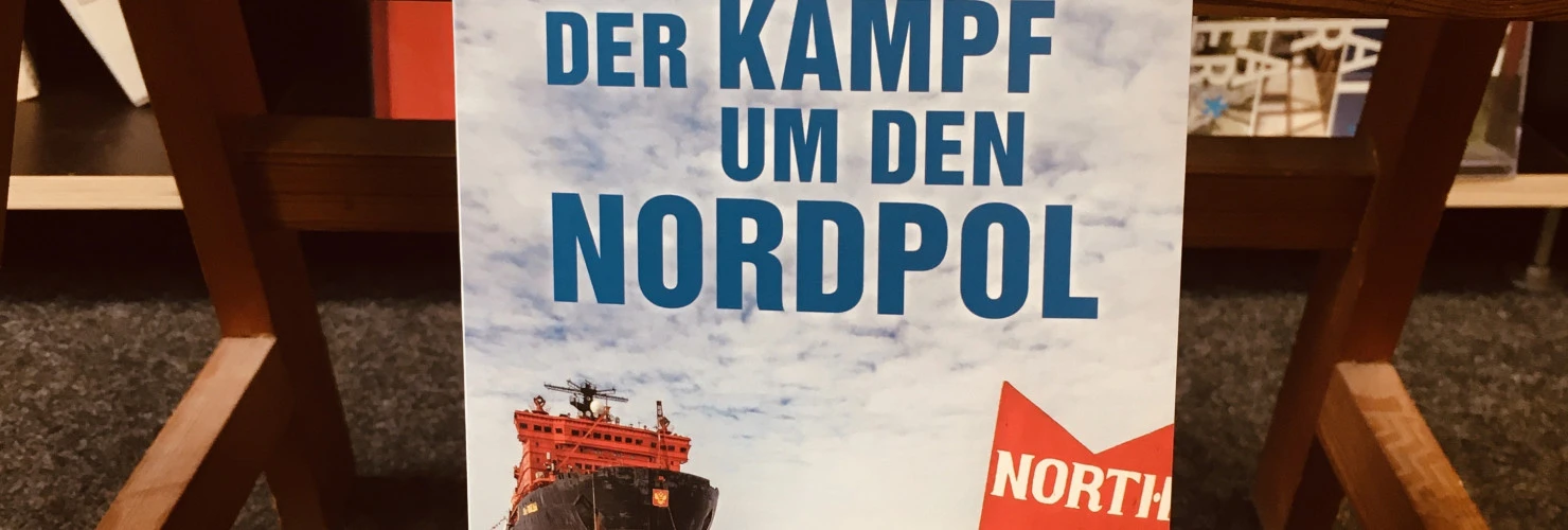 Ein Bild des Buches: " Der Kampf um den Nordpol- Die Arktis, Der Klimawandel und die Rivalität der Großmächte" von Michael Paul mit dem Hintergrund eines Bücherregals.  